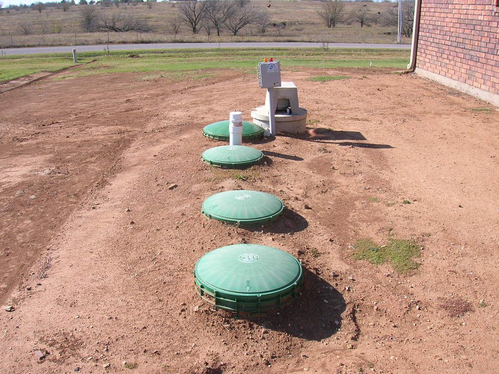 Completed aerobic septic system with tank risers and control panel installed behind a home near Granbury, TX